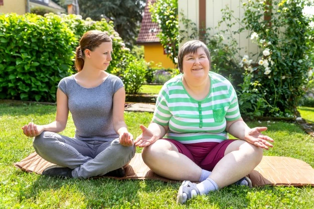 Disabled woman sitting outside on mat with carer practicing meditation
